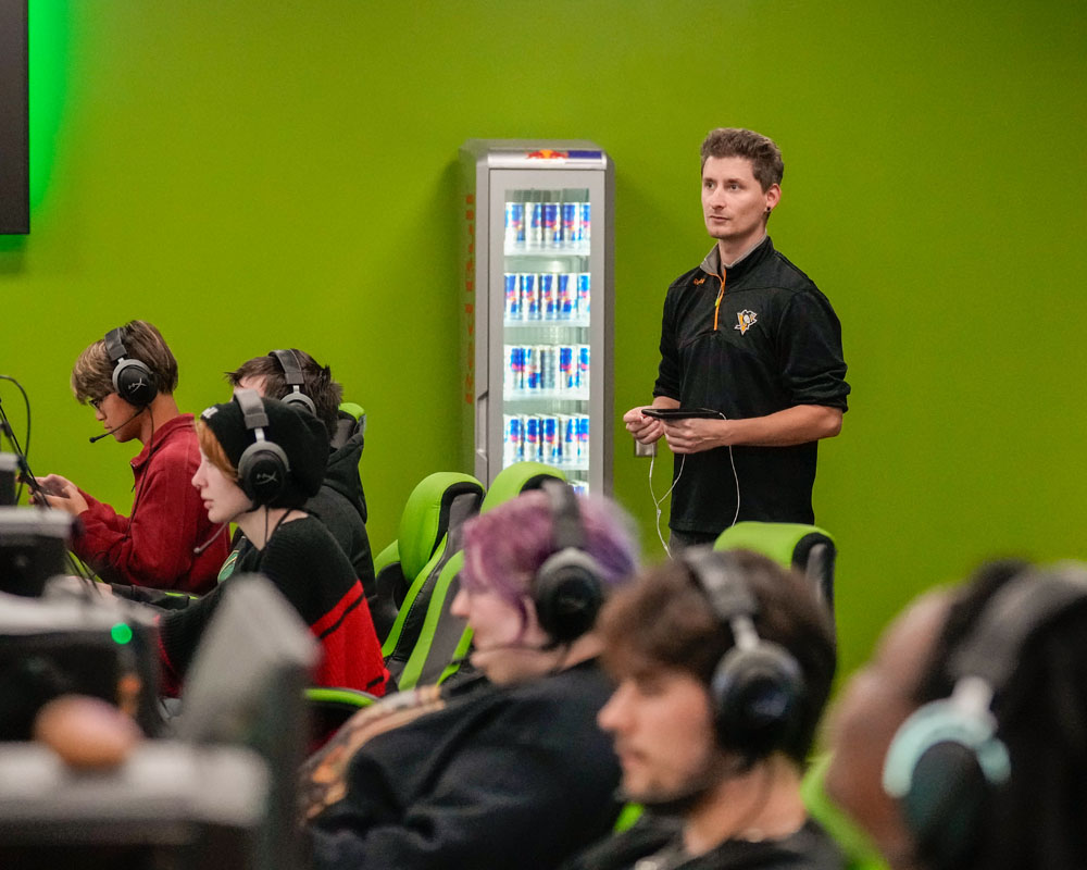 Esports students play a game while a man observes.