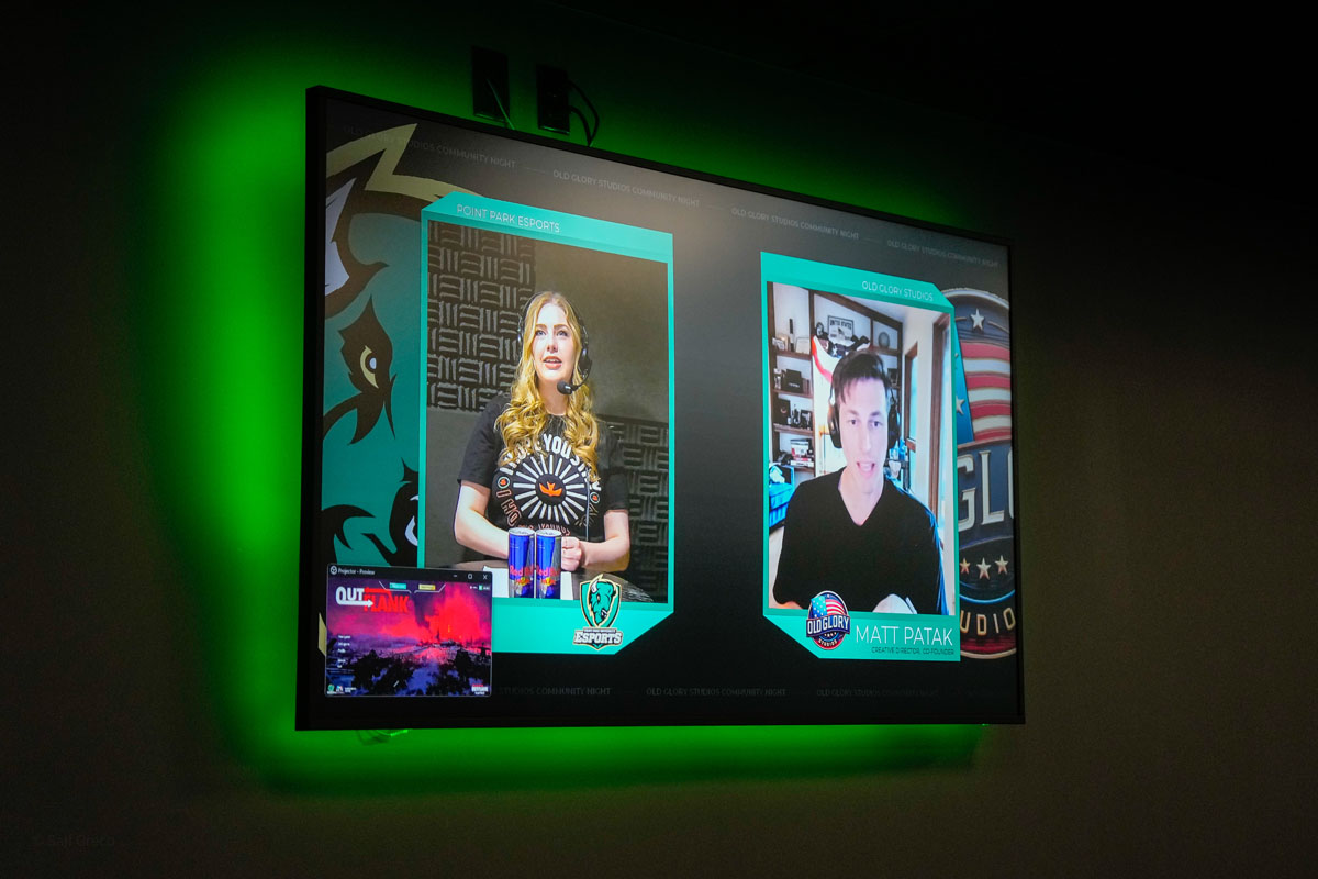 A screen contains two video boxes: one with a student announcer and another with a man. 