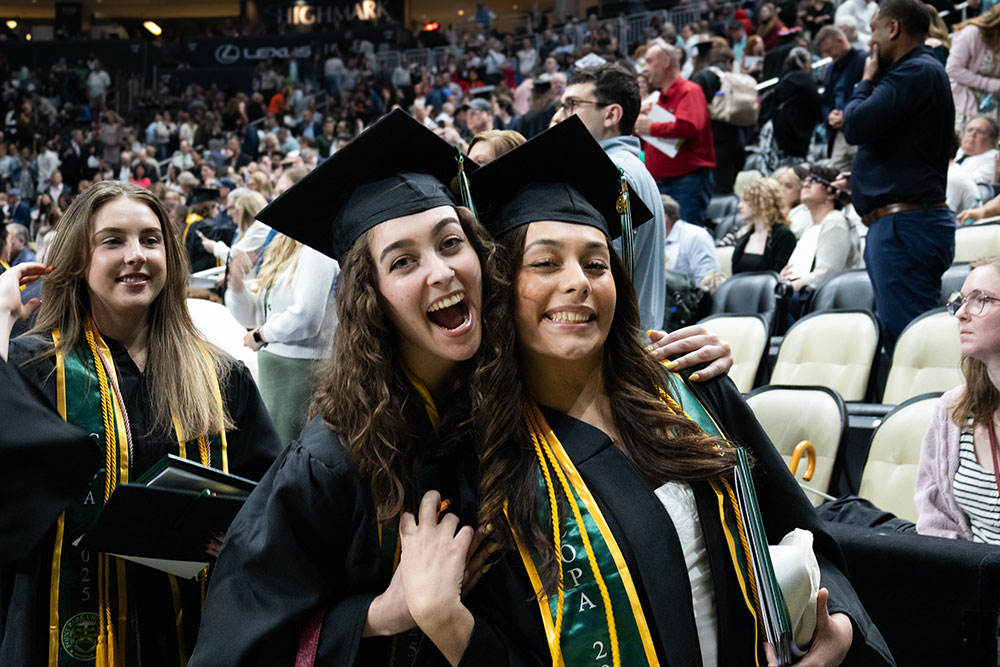 Two female graduating students hug.