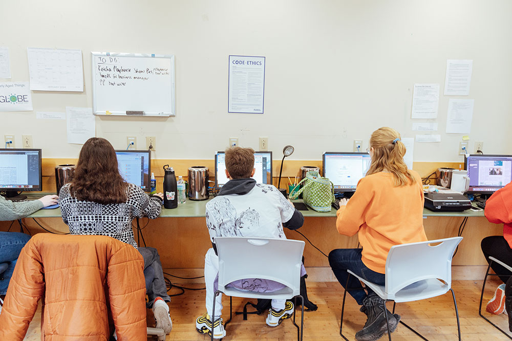 Three students sit facing computers.
