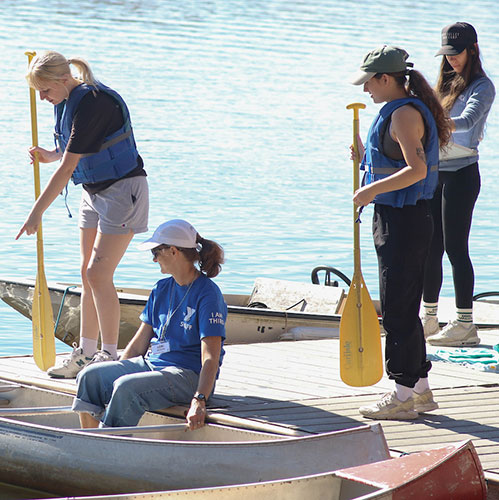 Four students wear life jackets and stand on a lake dock.