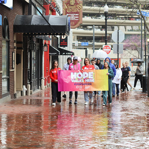 People walk through Market Square holding a sign that reads Out of the Darkness.