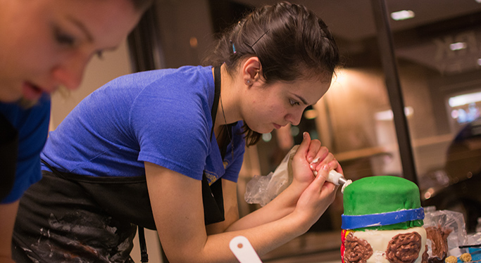 A student decorates a cake with an icing bag during the cake-off, Point Park's annual cake decorating competition.