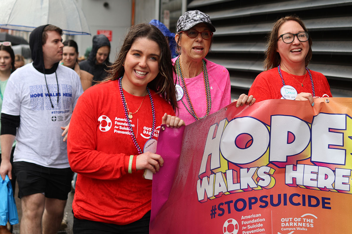 People walk down a street carrying a sign that reads "hope lives here."