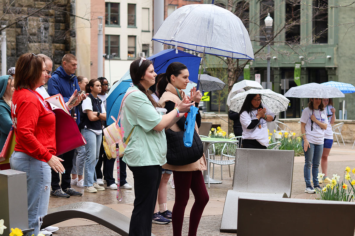 People stand holding umbrellas in Village Park.