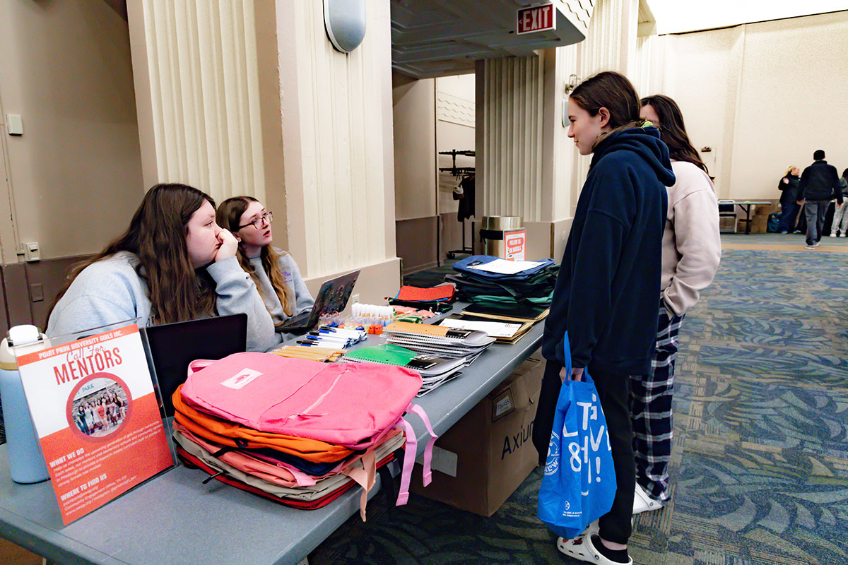 Two students sit behind a table full of school supplies.
