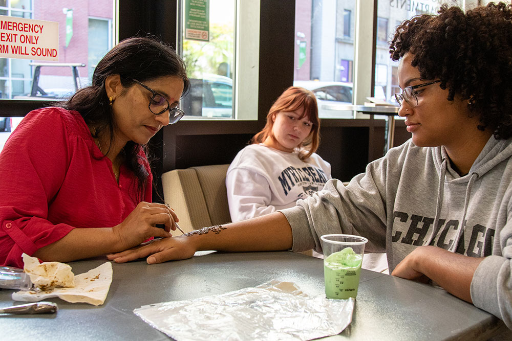 A woman draws a henna tattoo on a student's hand.