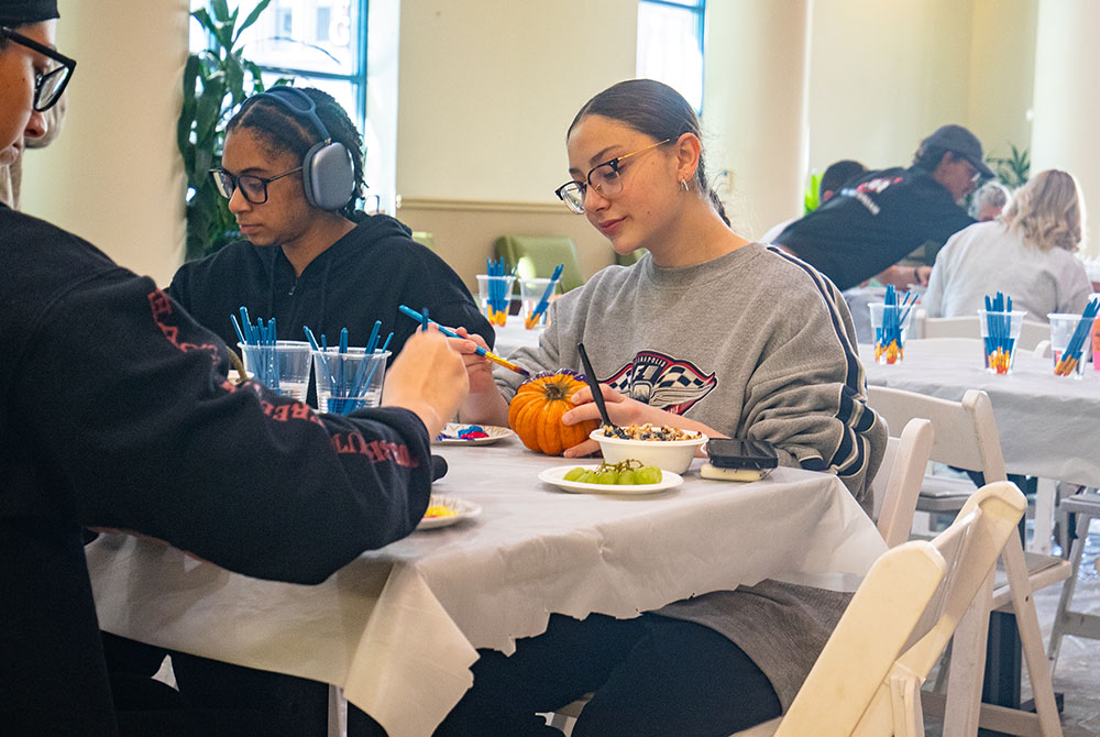 Students sit at a table painting pumpkins.