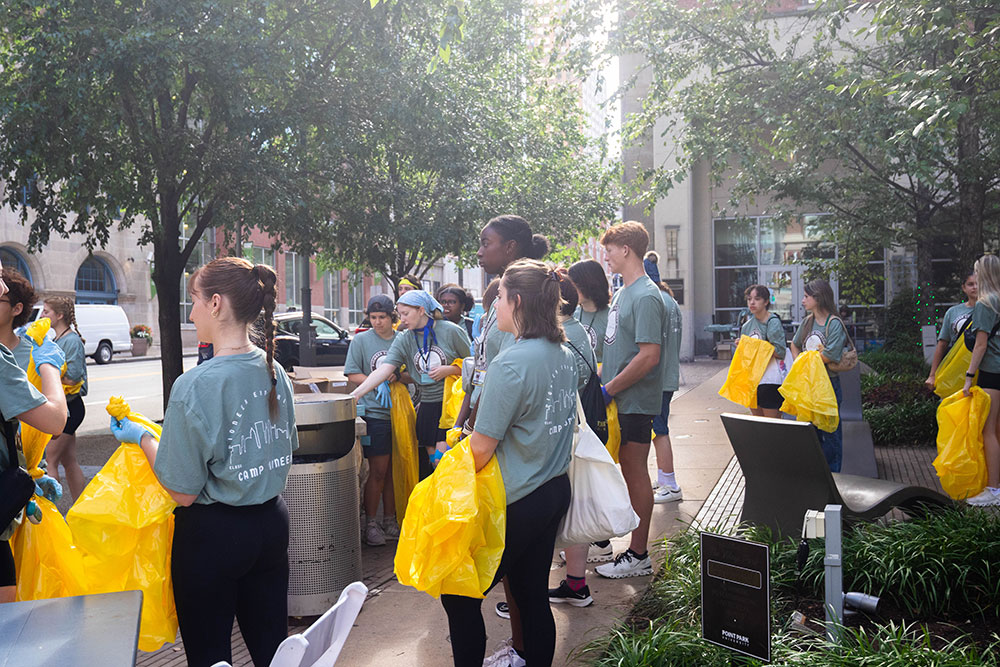 Students gather in Village Park holding yellow trash bags and wearing blue gloves.