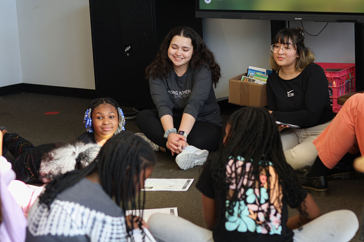 Two college girls sit on the floor in a circle with 