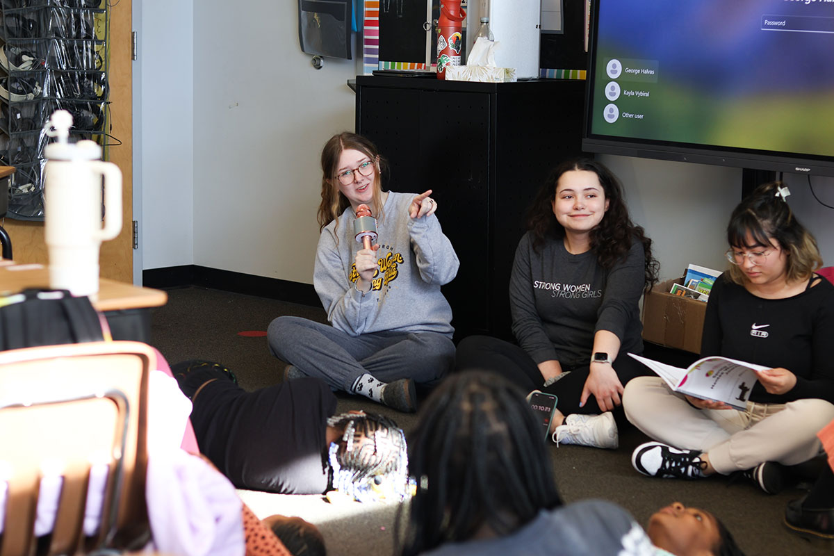 A college student sitting on the floor speaks into a microphone.