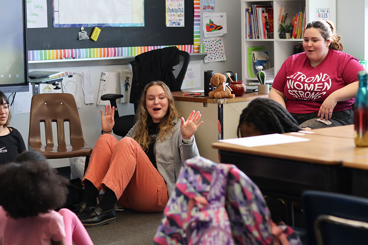 A woman sitting on the floor throws her arms in the air.