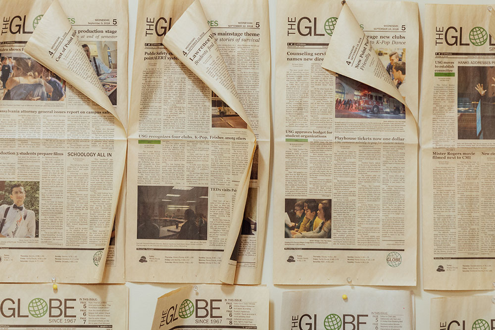 Front pages of a newspaper are pinned to a wall.