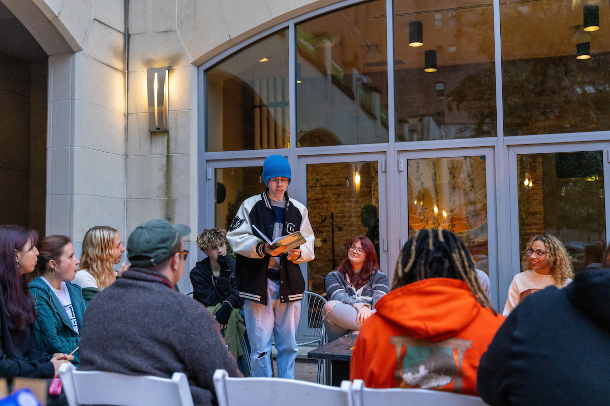 A student reads while others sit around a firepit.