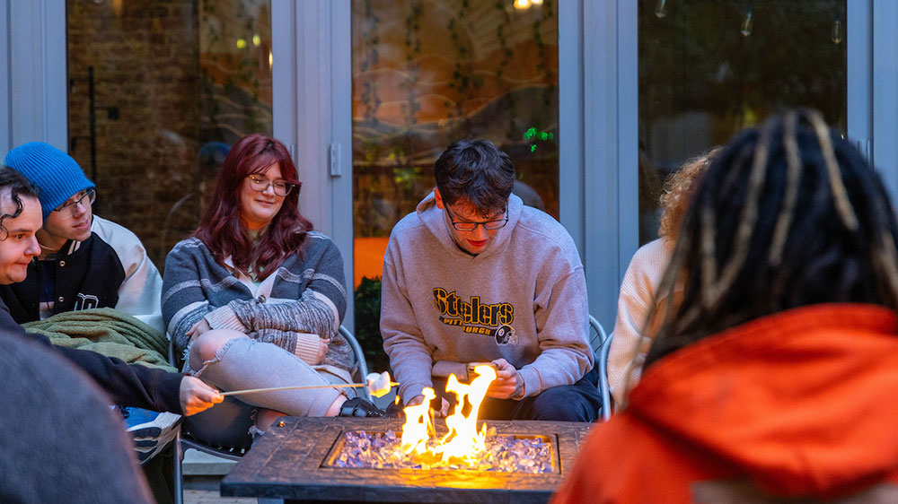 A student reads from his phone while others roast marshmallows in Village Park. 