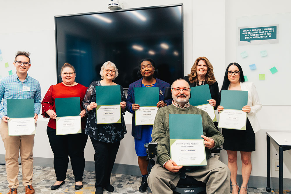 A group of graduates stand together holding their certificates.