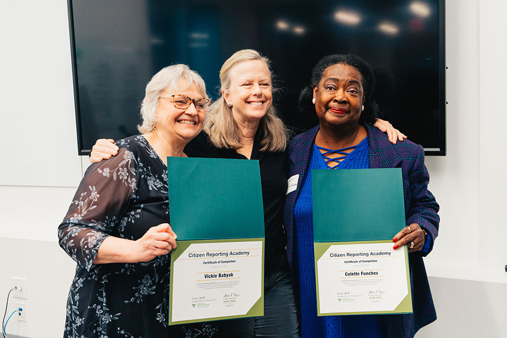 Three women stand together smiling, two are holding graduation certificates