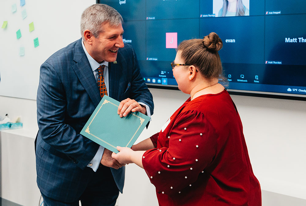 Chris Brussalis shakes a female graduate's hand while handing her a graduation certificate.