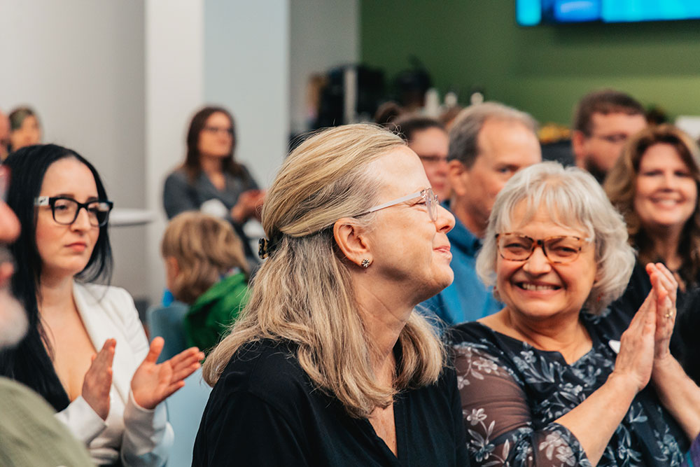 A woman in an audience smiles while others clap and look at her.