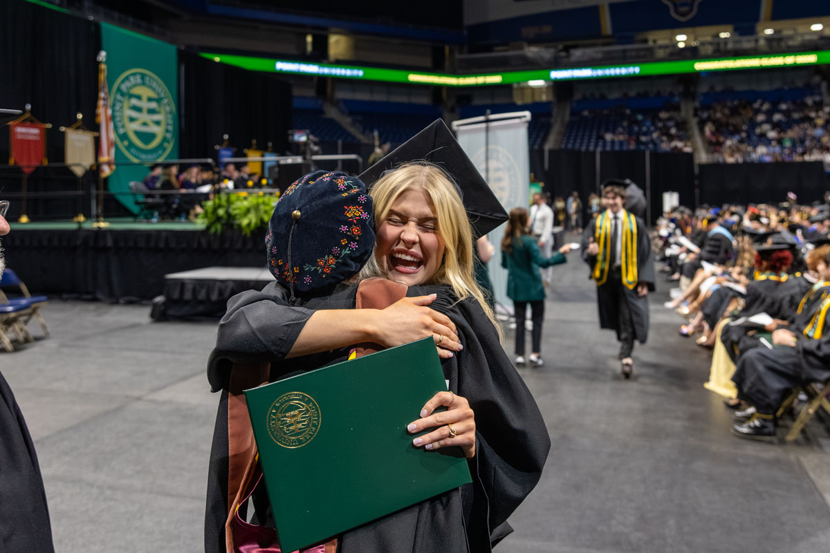 A woman hugs her professor with her diploma cover in her hand.