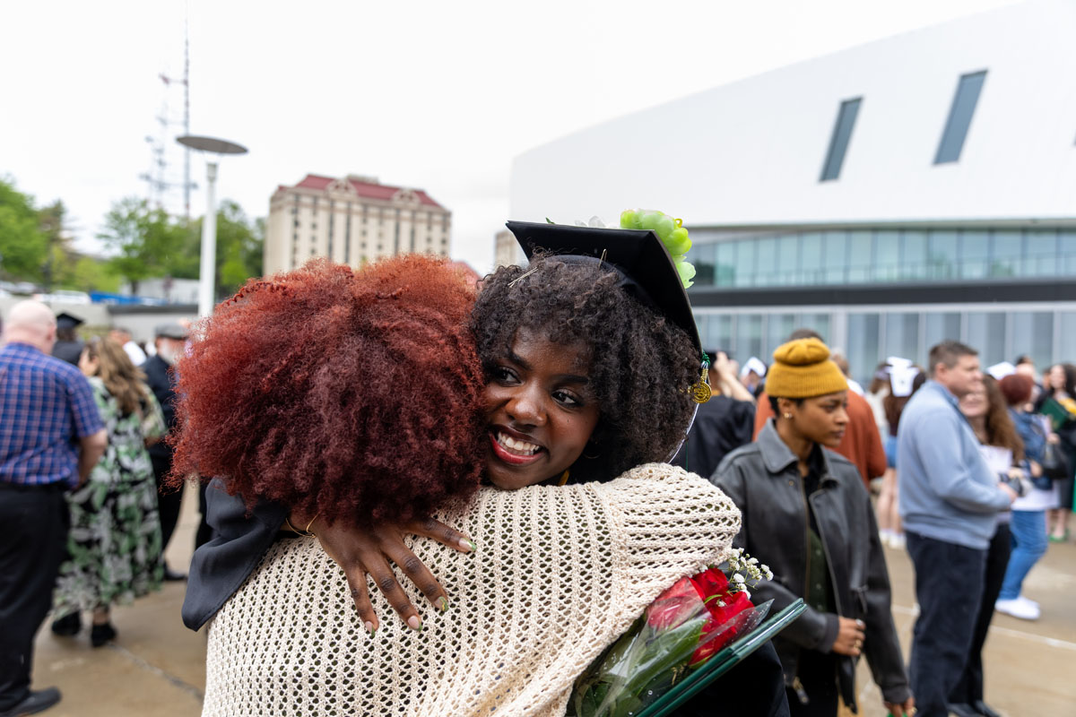 A graduate hugs a friend outside the center.
