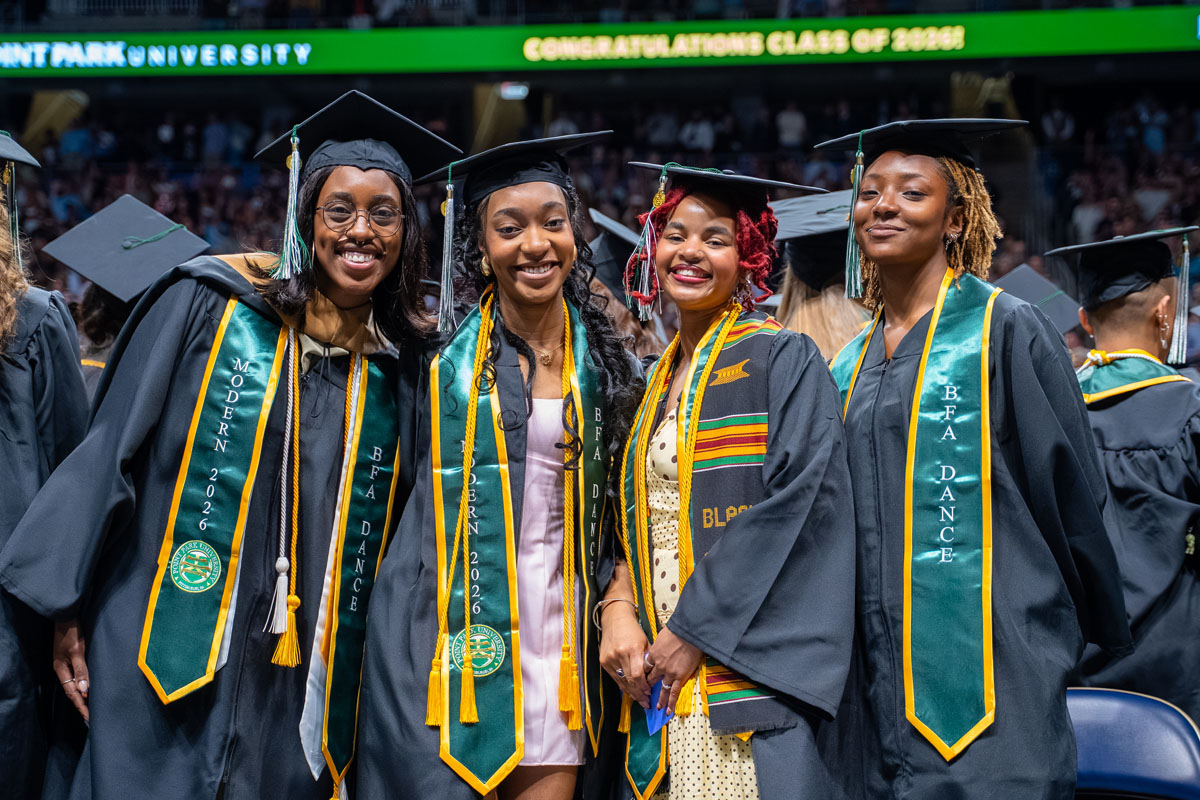 Four graduates pose in a line for a photo.