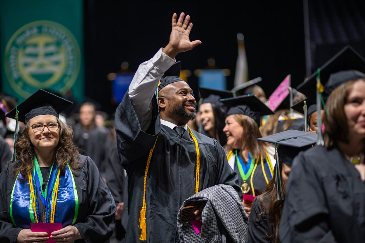 A graduate waves at his family in the crowd.