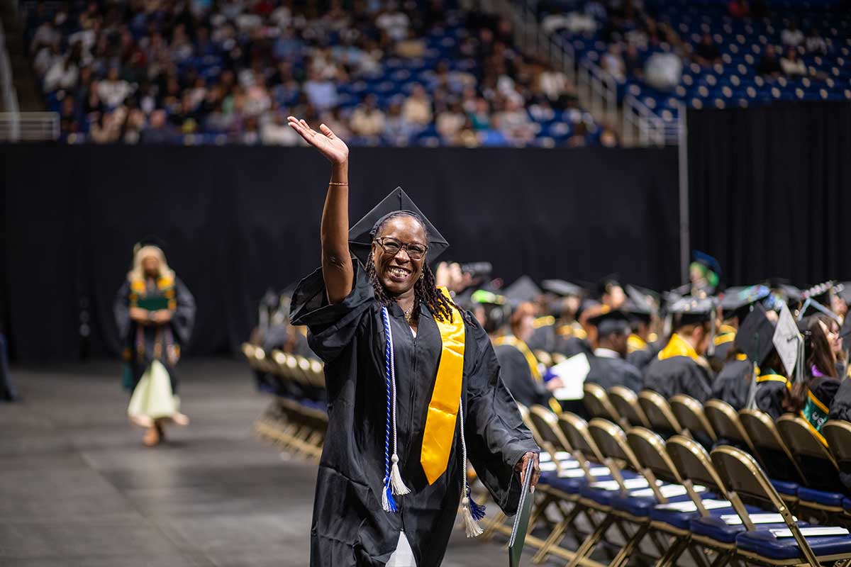 A graduate waves as she walks.