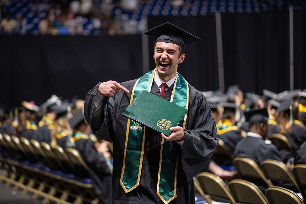 A male graduate points to his diploma as he walks back to his seat.