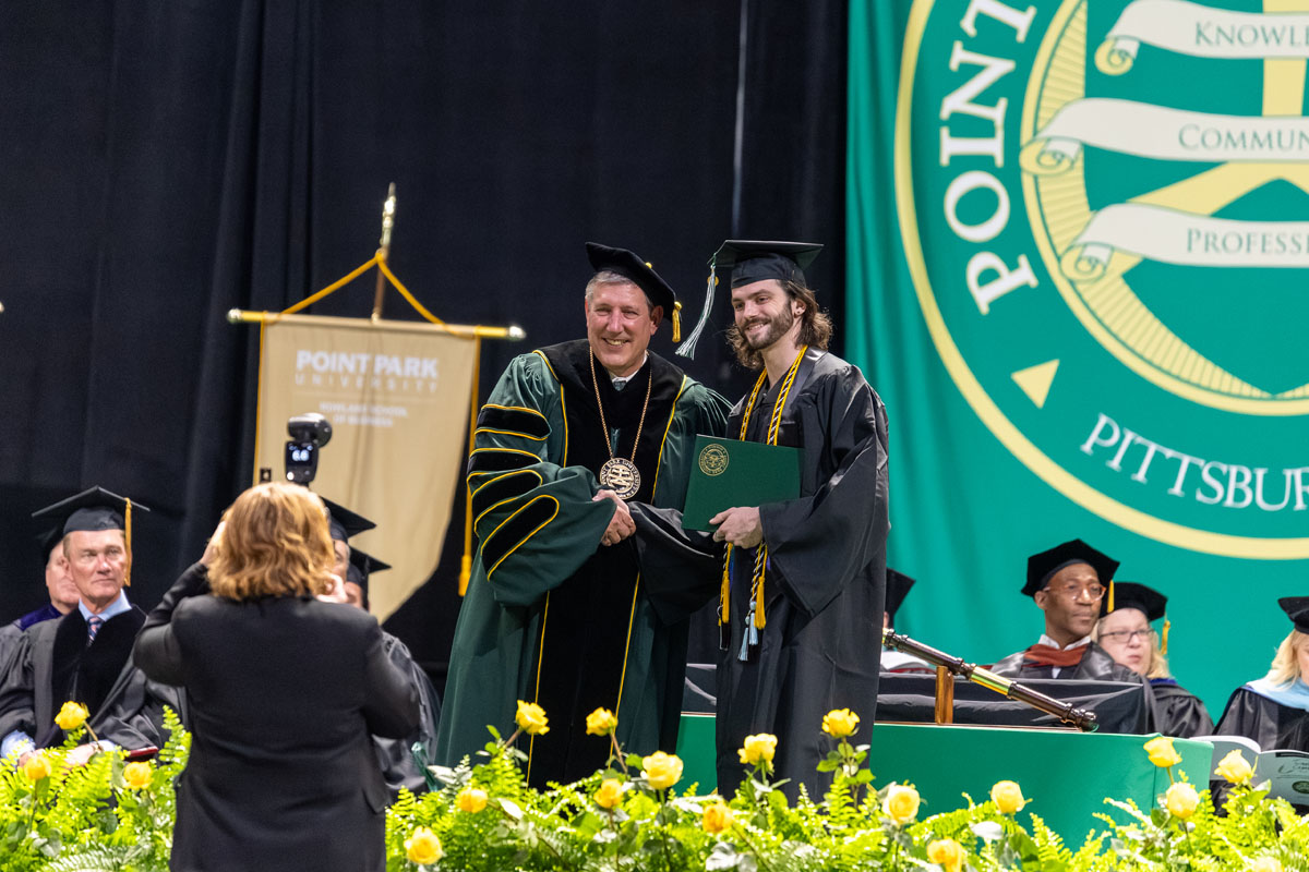 A student receives his diploma and shakes the president's hand.