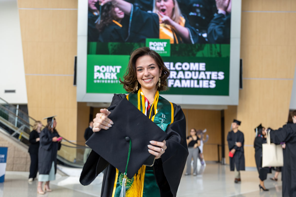 A graduate holds her cap up to the camera.