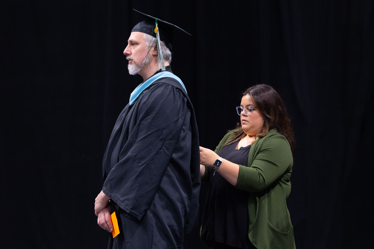 A graduate receives his hood on stage.