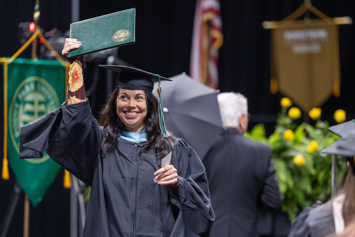 A graduate holds her diploma up to show people.