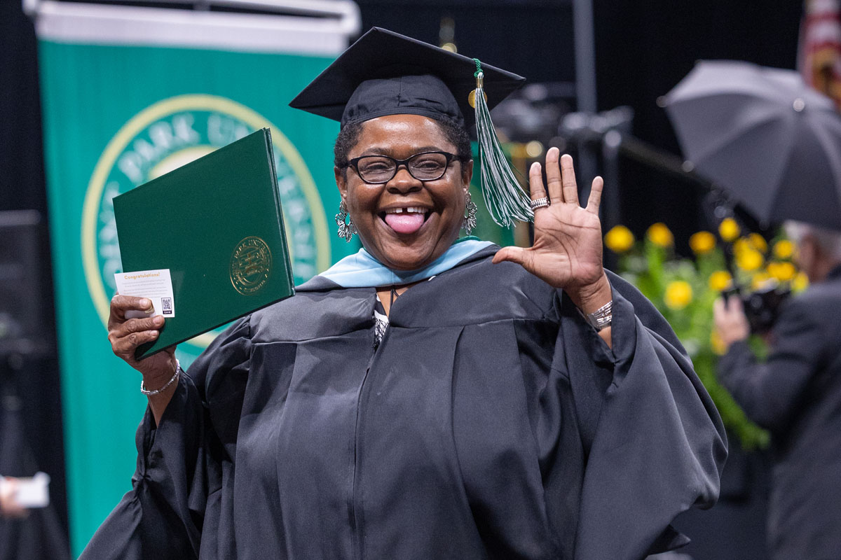 A graduate smiles at the camera with their diploma.