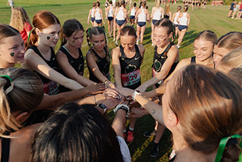 Women on the cross country team put their hands together in a circle.