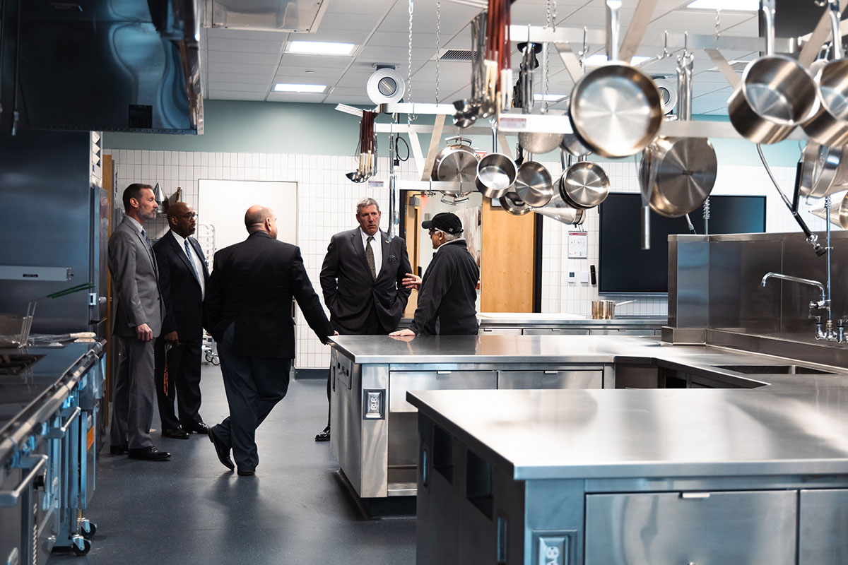 Five men stand in an industrial kitchen, talking.