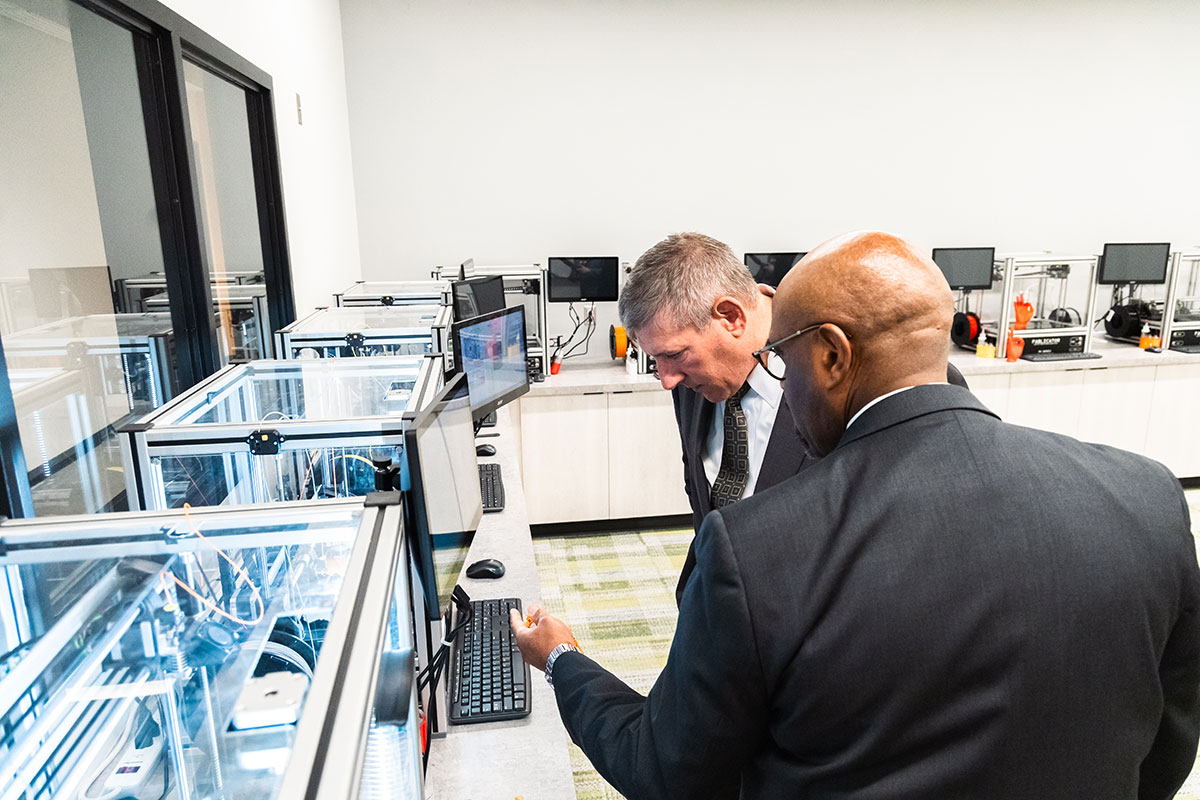 A man shows another man a 3D printer.