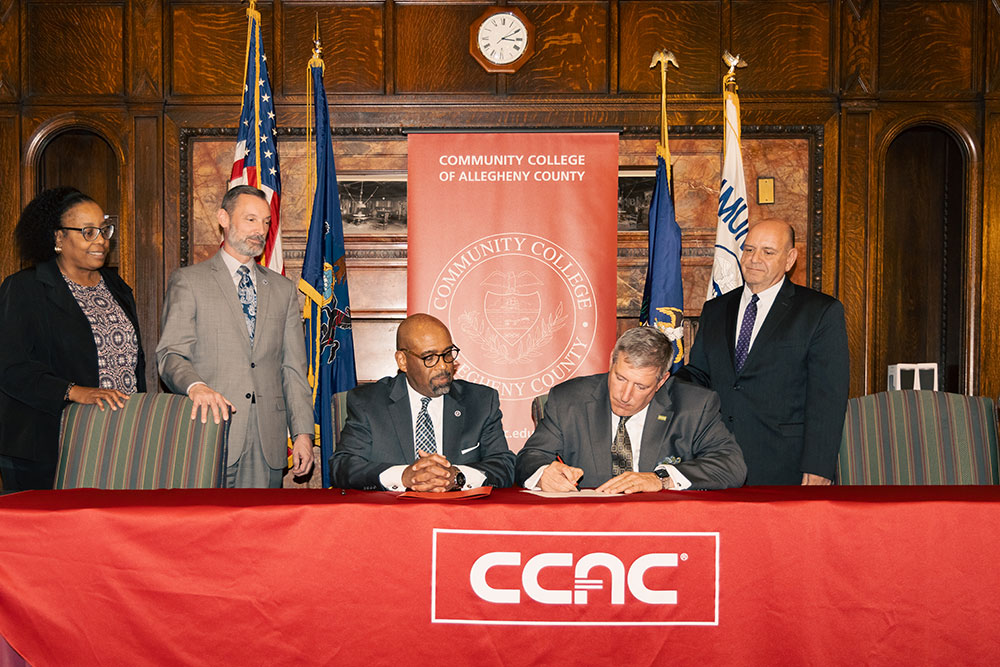 Two men sit at a table signing a document.