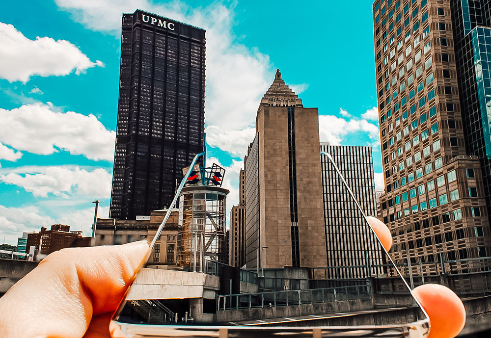 Pictured is a hand holding a cell phone with the Pittsburgh skyline reflecting on it. Photo by Nathaniel Holzer.
