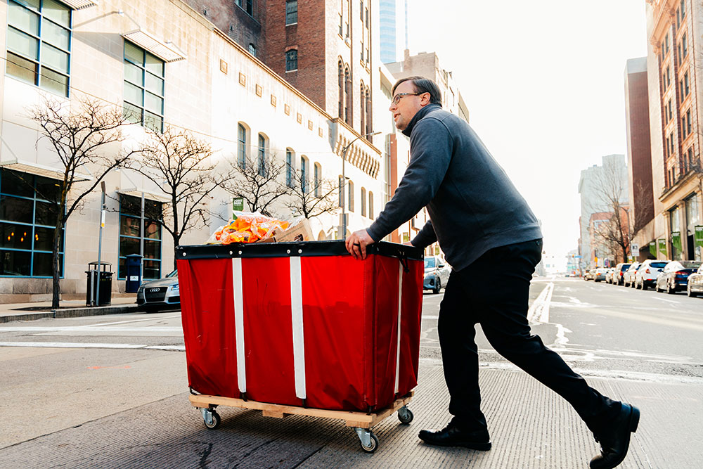 A man crosses a street pushing a red bin.