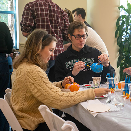 Two people paint pumpkins at a table.