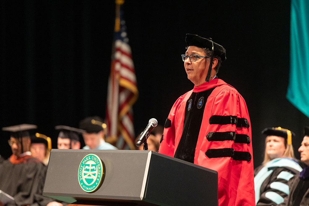 A man in red academic regalia stands at a podium. 