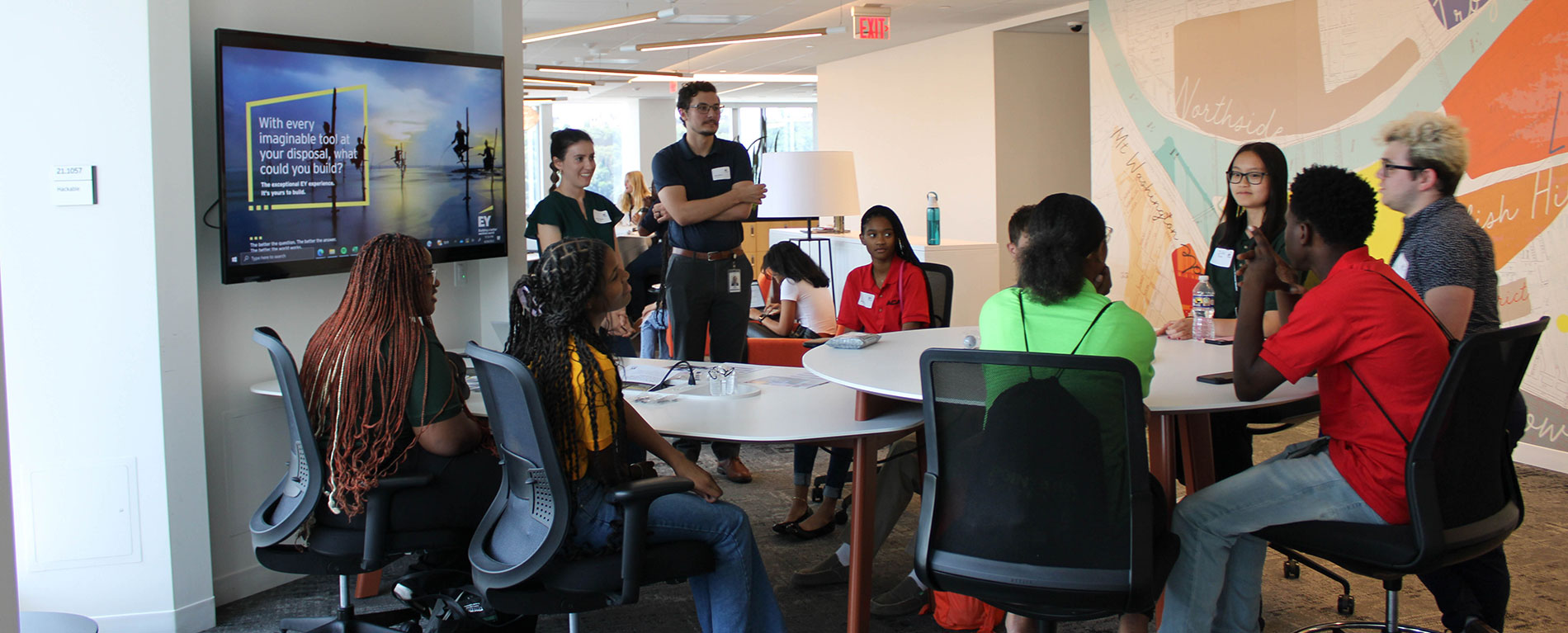 A group of students sit around a table with adults who are teaching them