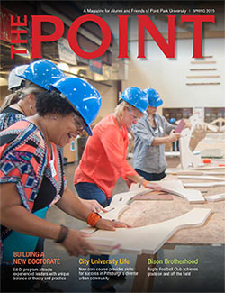 Image of the cover of The Point, the magazine for alumni and friends of Point Park University, showing doctoral students building wooden desks as a team-building activity.