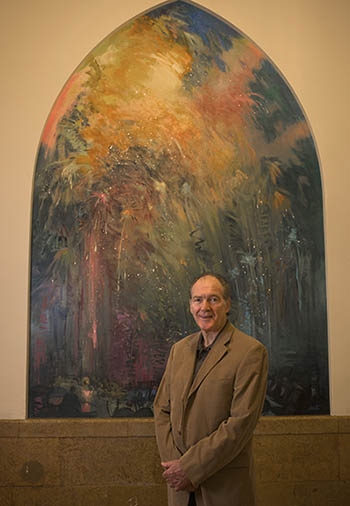 Pittsburgh artist Philip Salvato stands with his new mural of vibrant, free-flowing colors representative of fireworks, with an orchestra depicted at the base of he painting. The mural occupies an arch-shaped niche in the historic staircase in Lawrence Hall. | Photo by Martha Rial