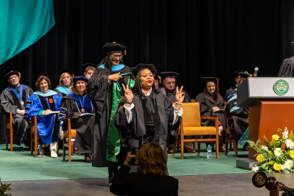 A student makes the peace sign as she waits to receive her hood.