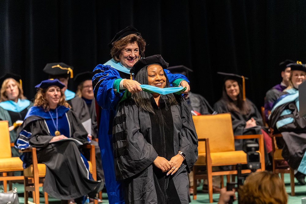 A graduate gets hooded by Linda Hippert.