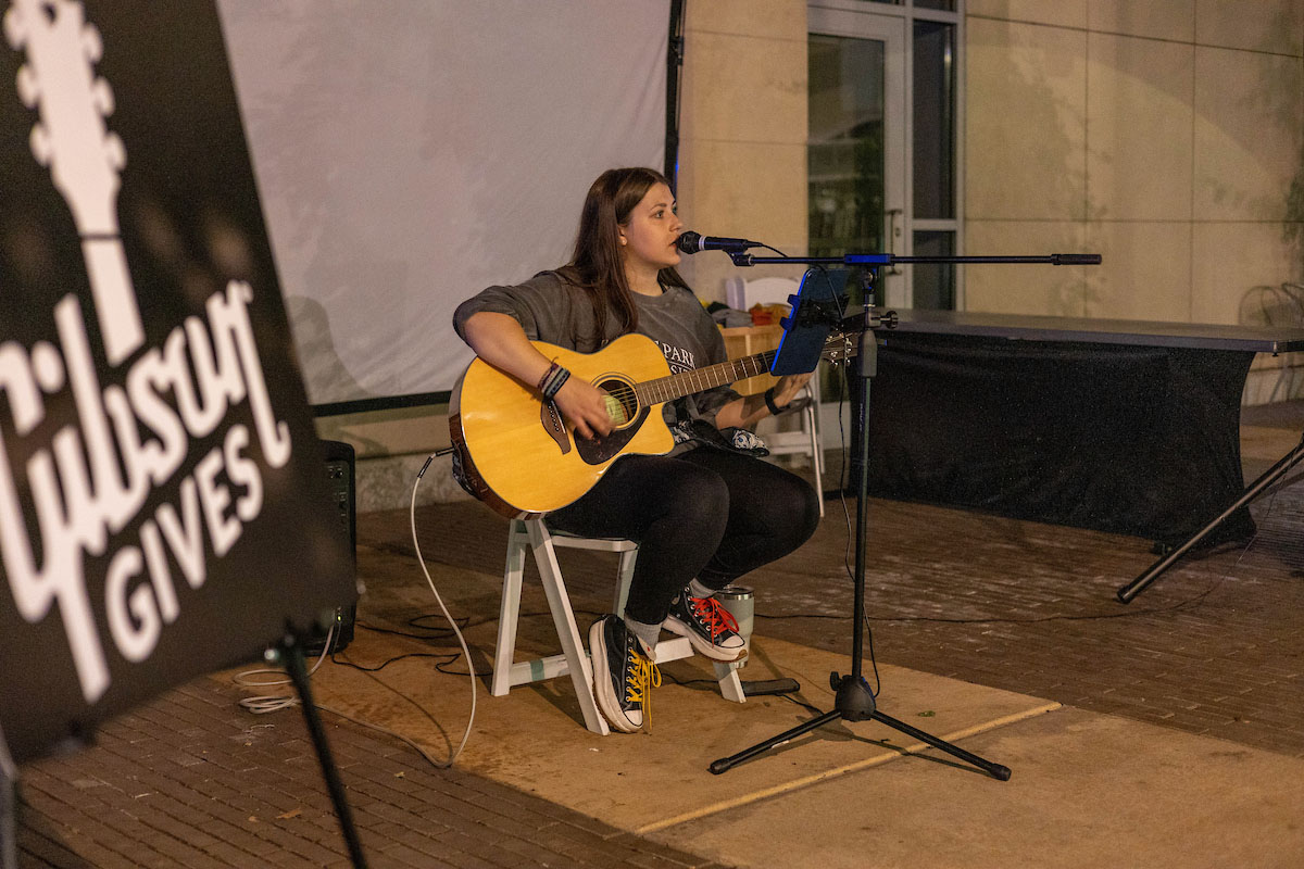 A student plays guitar in Village Park. 