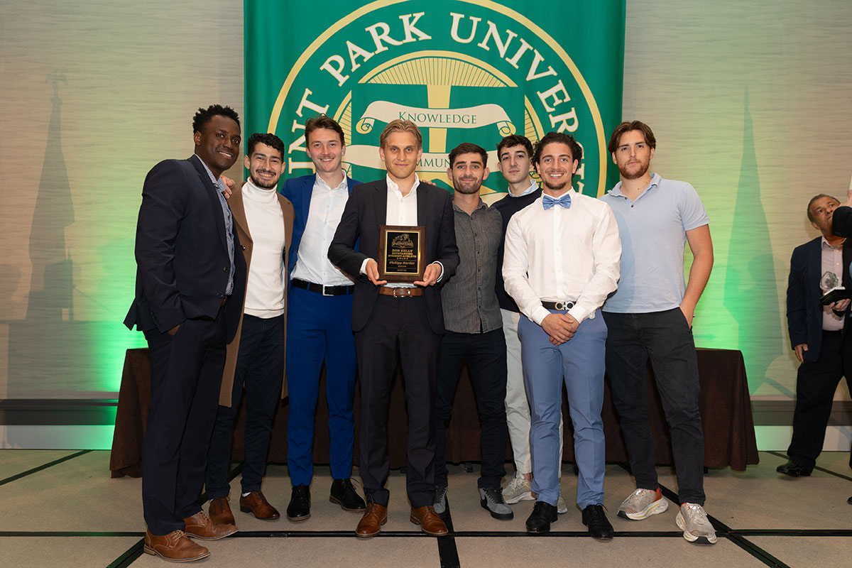 A group of students stand around one holding an award.