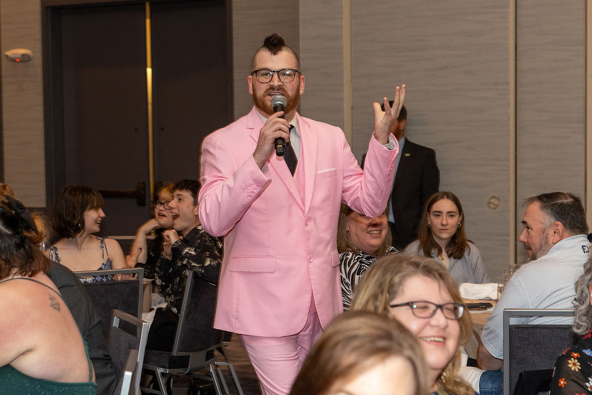 A man in a pink suit speaks into a microphone